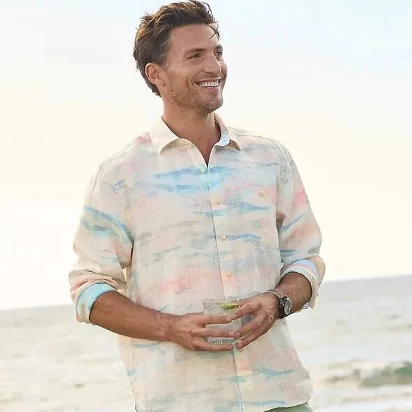 Man wearing a colorful shirt and light green pants standing on a beach.