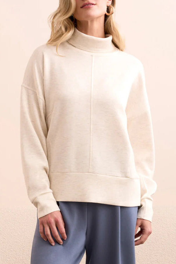 Person wearing a white sweater and light blue pants standing in a room with a beige sofa.