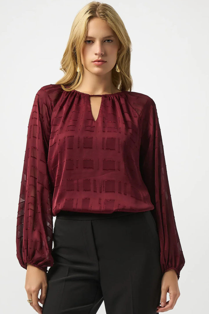 Woman wearing a burgundy patterned blouse with long sleeves on a white background