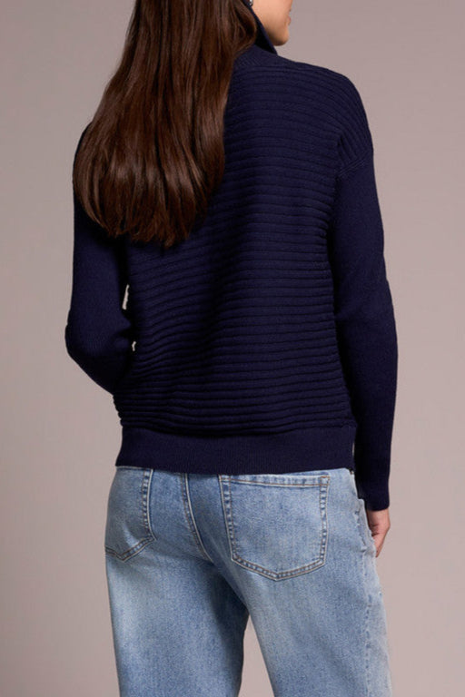 Person wearing a navy sweater and light blue jeans with brown shoes on a beige background