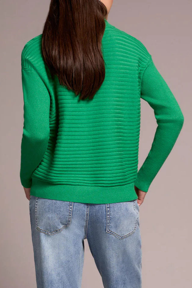 Person wearing a green sweater and blue jeans against a beige background