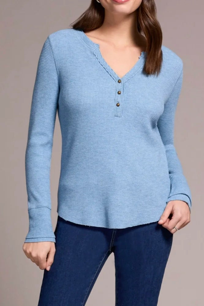 Woman wearing a light blue long-sleeve top and dark blue jeans with brown boots on a neutral background