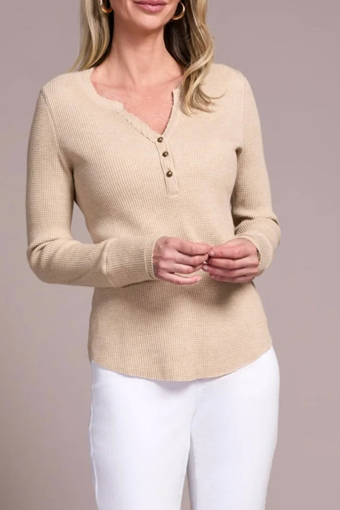 Woman wearing a beige sweater and white pants against a plain background