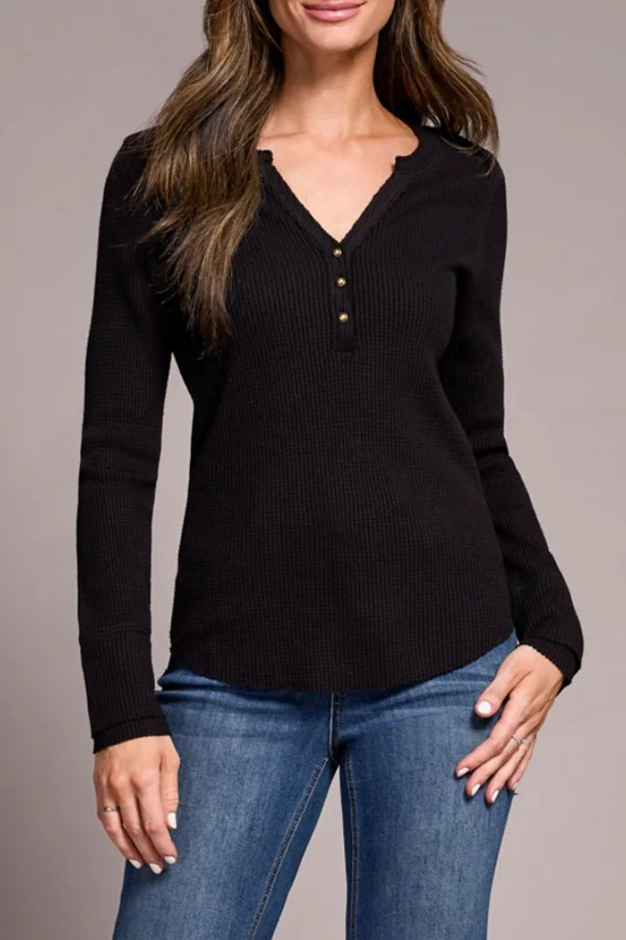 Woman wearing a black long-sleeve top and blue jeans with brown boots on a gray background