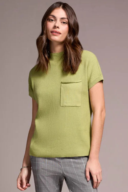 Woman wearing a green ribbed sweater and gray checkered pants against a plain background