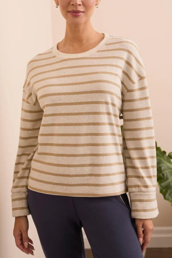 Woman wearing a beige and brown striped long-sleeve shirt and dark leggings indoors.