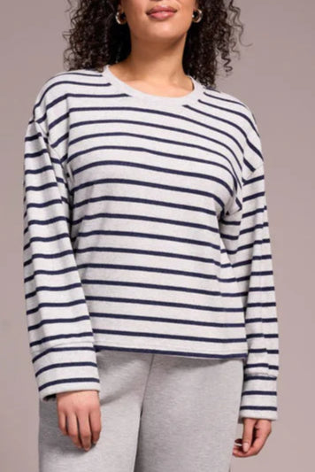 Woman wearing a striped sweater and gray pants against a plain background