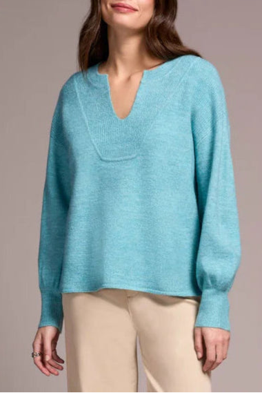 Woman wearing a light blue sweater and beige pants against a plain background
