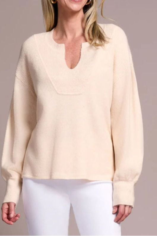 Woman wearing a light yellow sweater and white pants against a neutral background