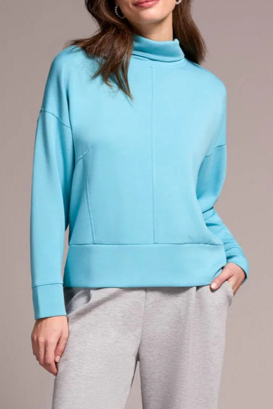 Woman wearing a light blue sweater and gray pants against a plain background